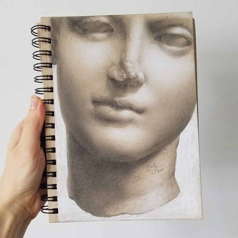Handholding a sketchbook featuring a detailed gray-scale drawing of a sculpture's face.