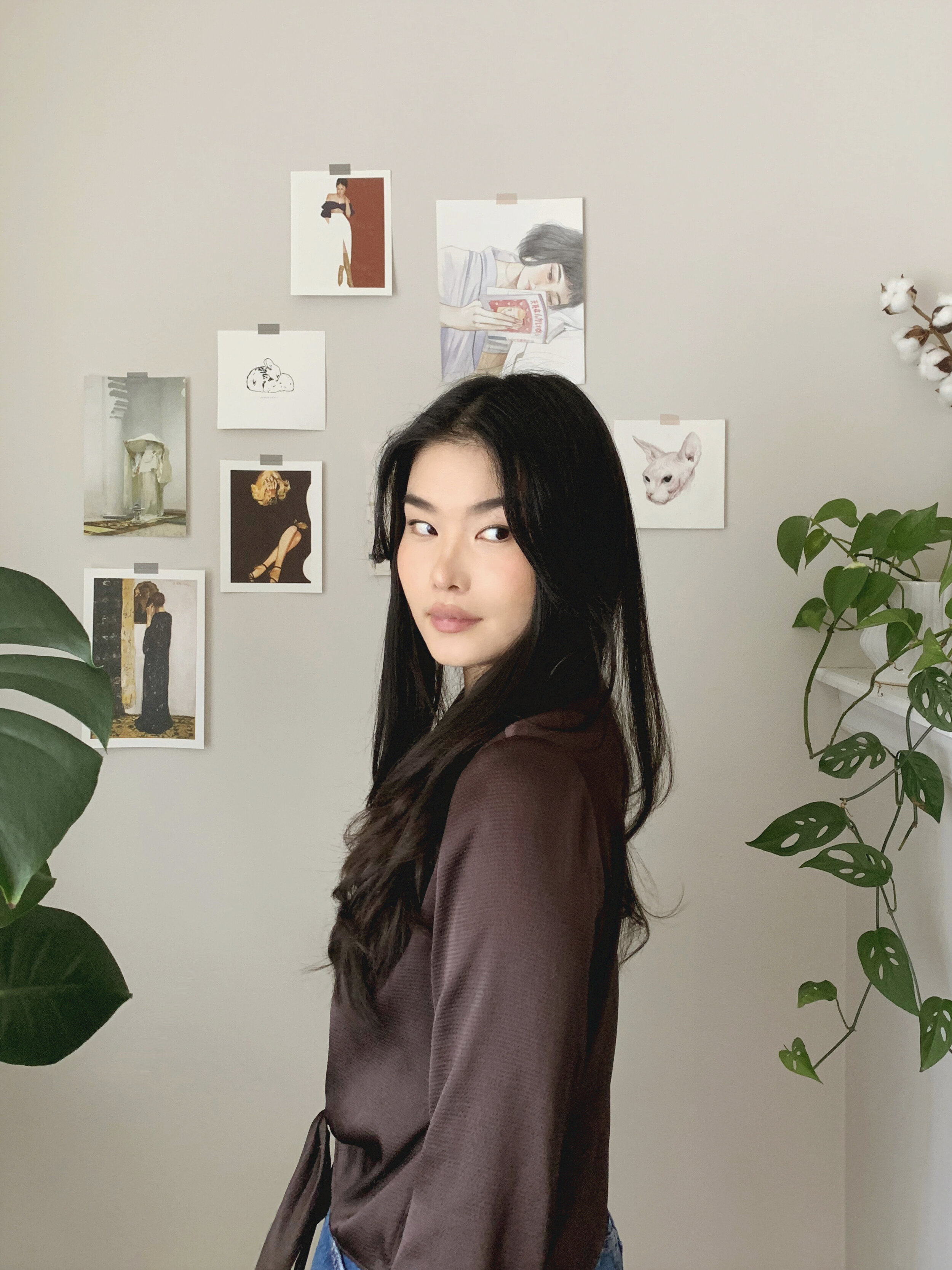 Young woman in stylish outfit, surrounded by art and plants indoors.