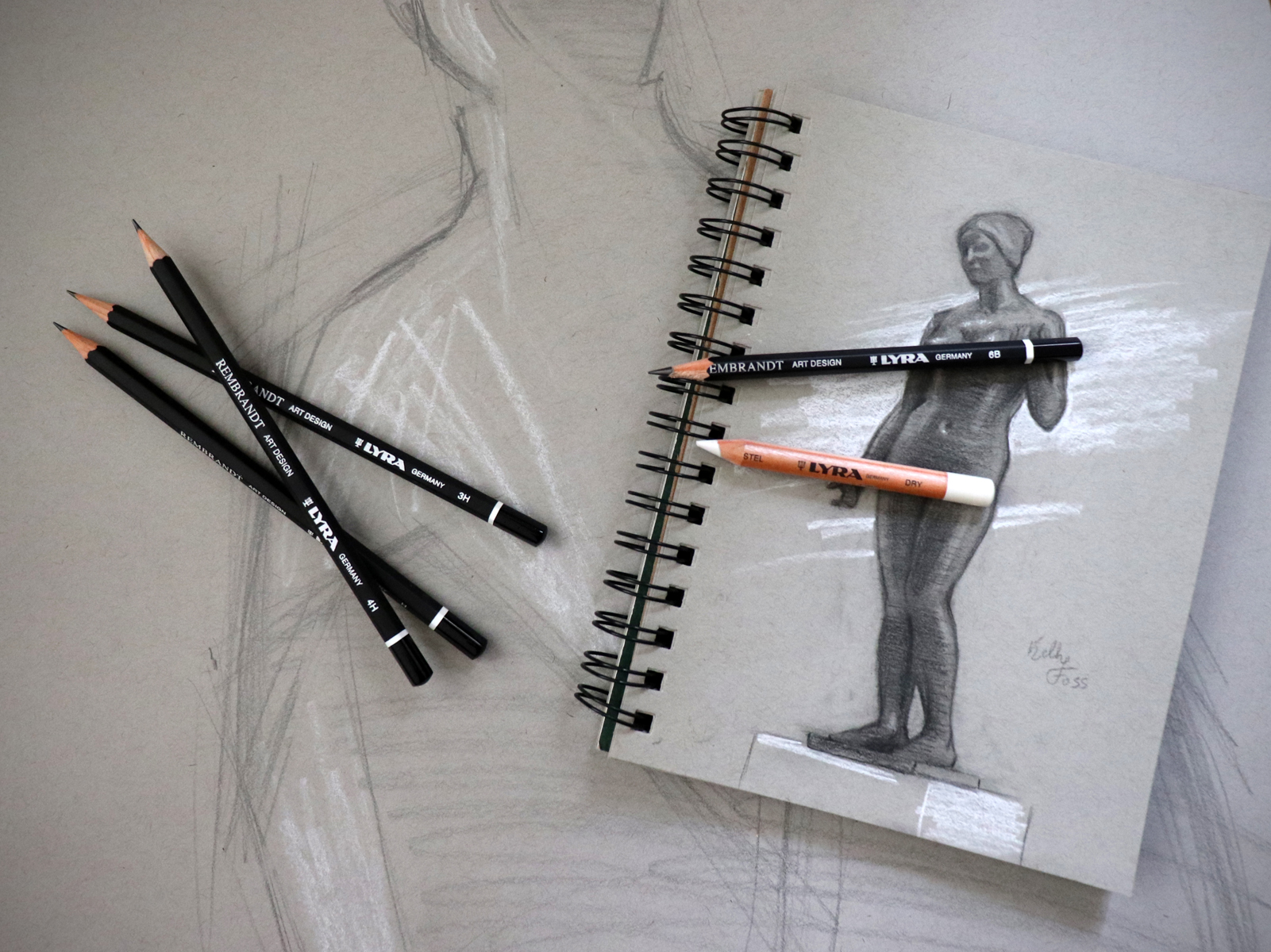 Art supplies with sketchbook and figure drawing tools on gray background.