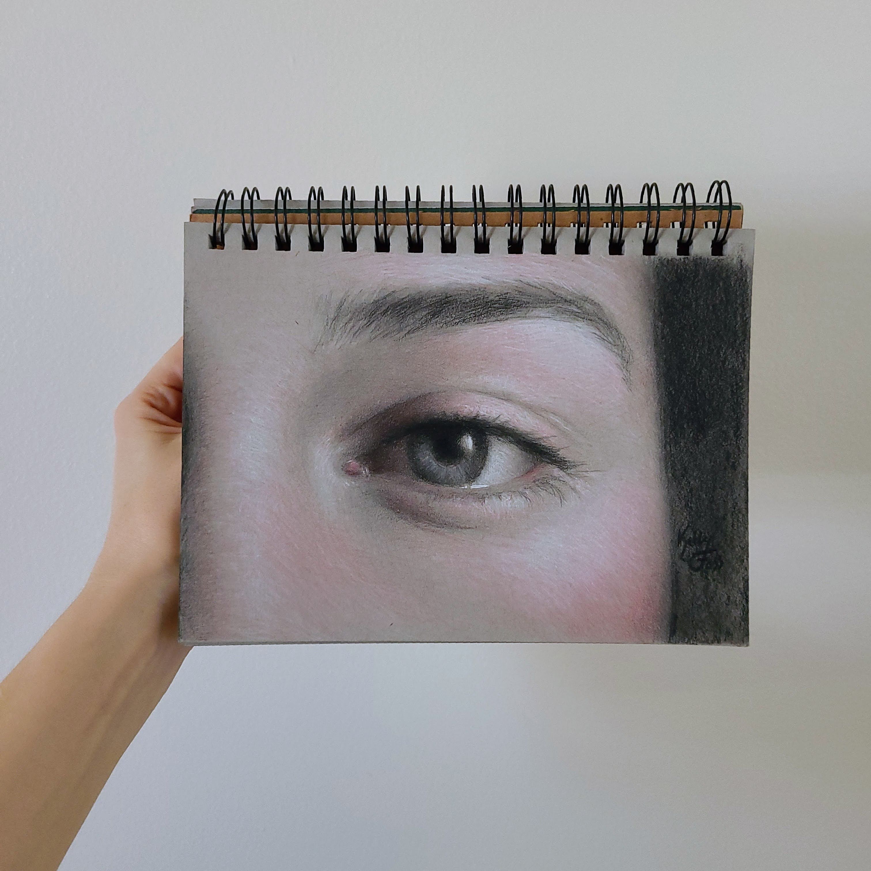 "Realistic eye drawing in sketchbook, showcasing detailed color pencil artwork."