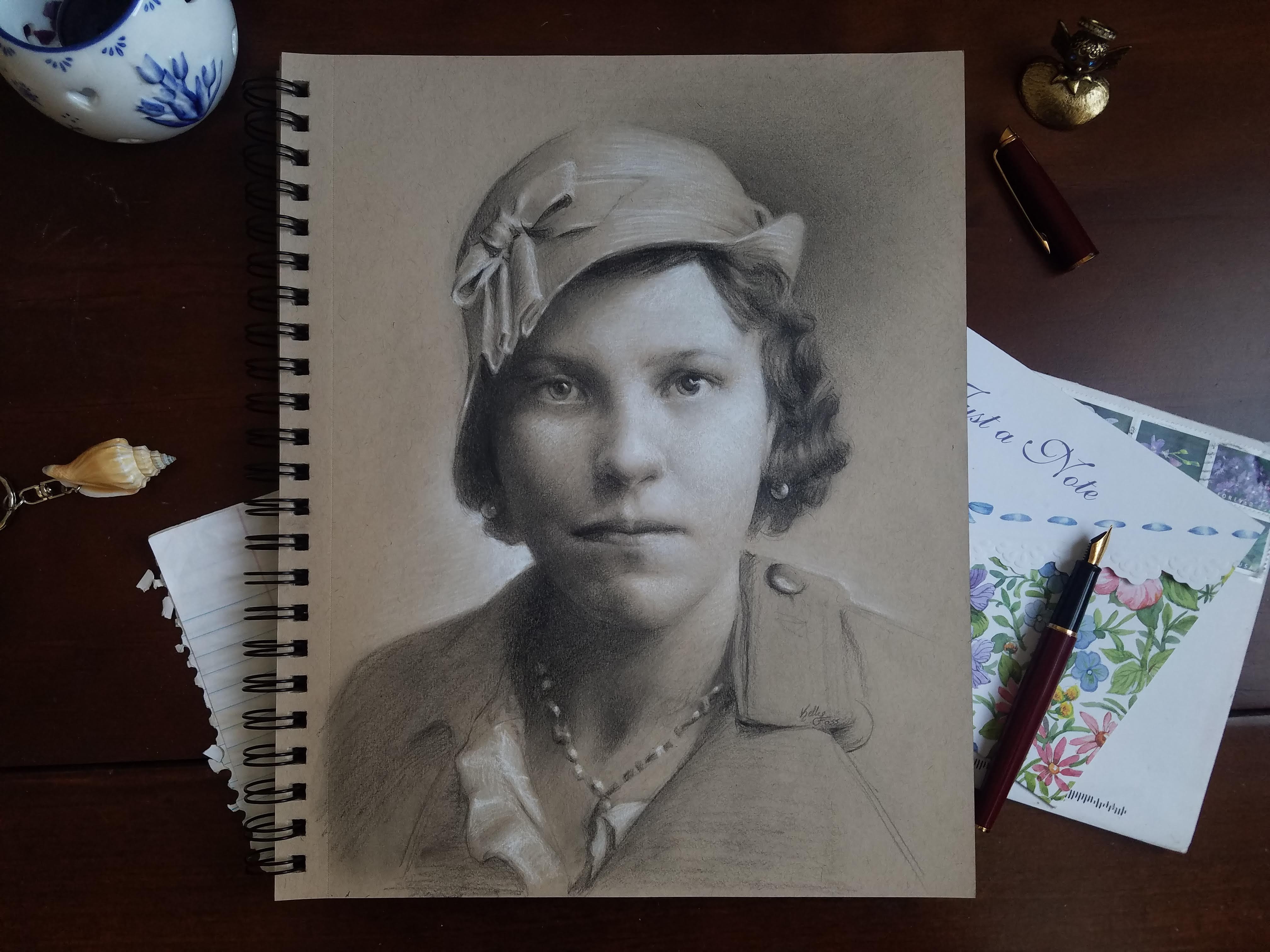 "Charcoal portrait of a young woman in vintage style hat on sketchbook."