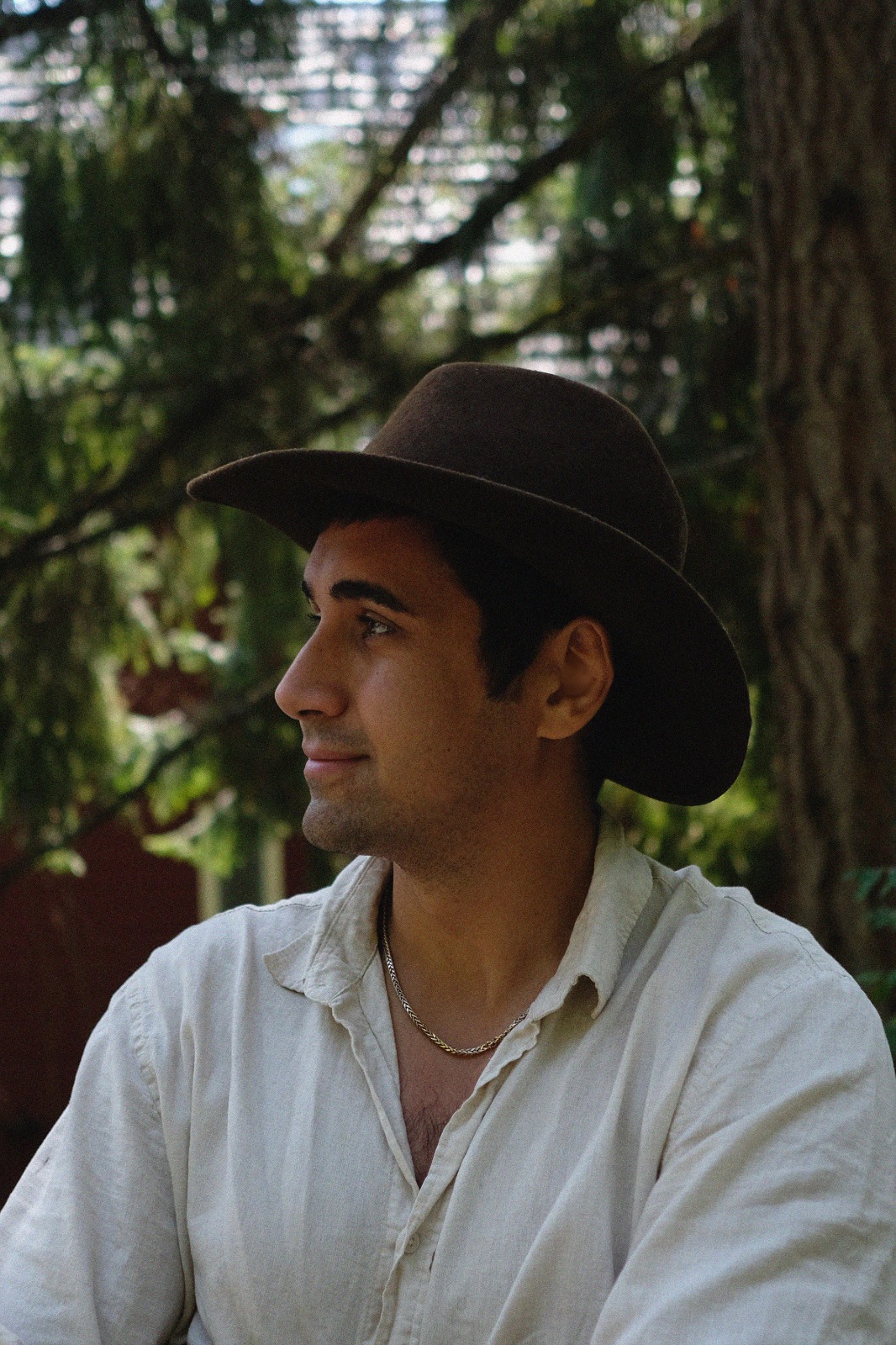 Young man in a hat sitting outdoors surrounded by trees.