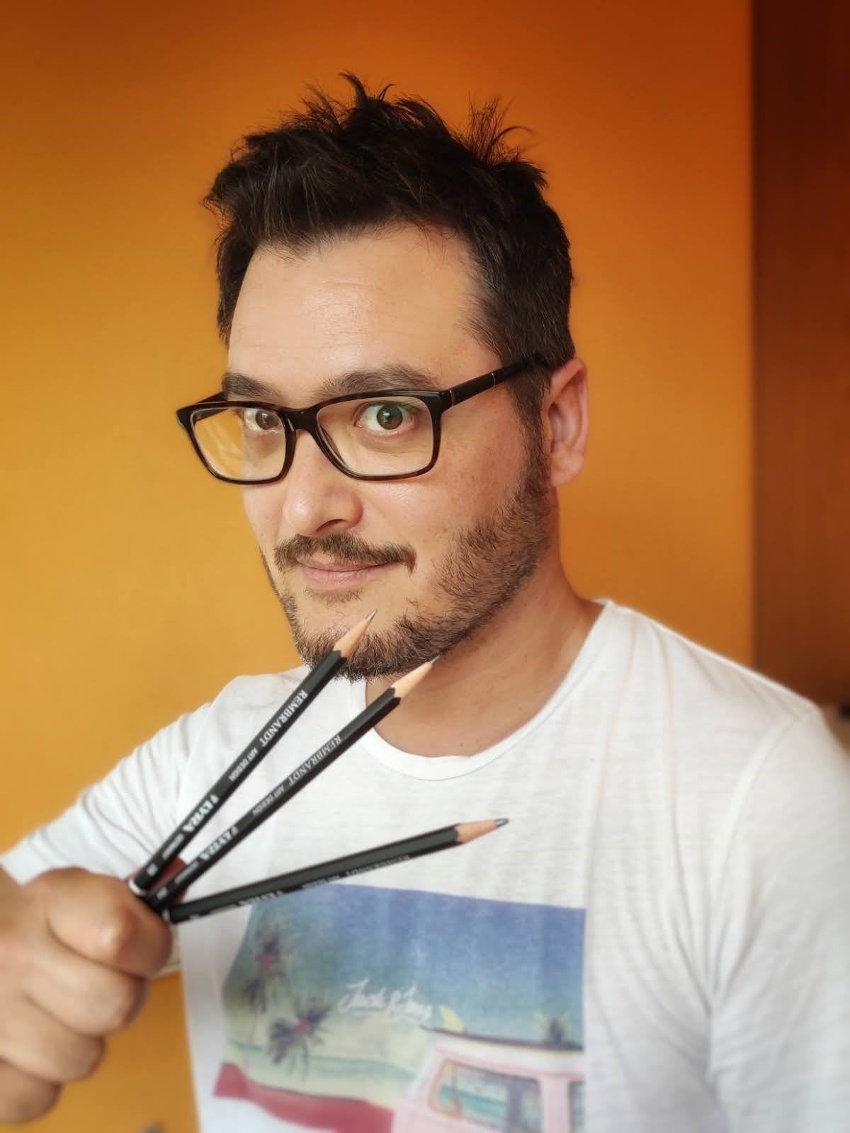 Man holding colored pencils with a playful smile against a bright orange background.