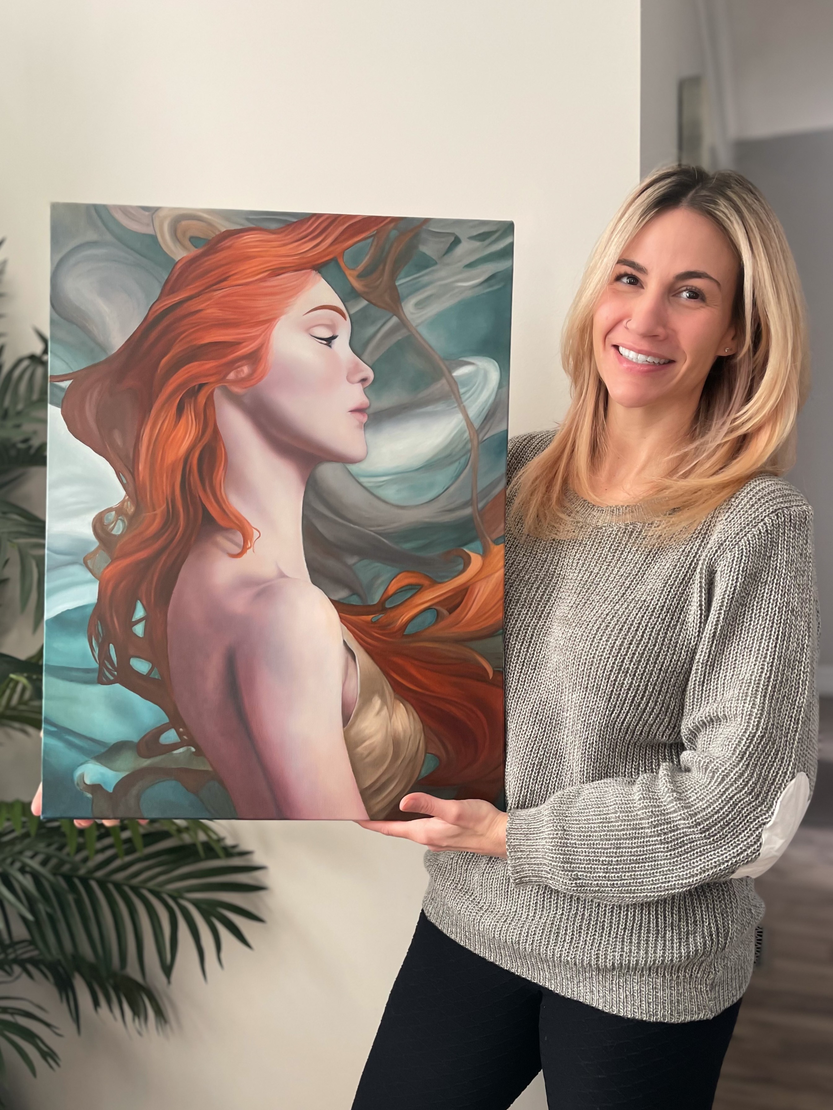 Woman proudly displaying a vibrant painting of a serene red-haired figure.