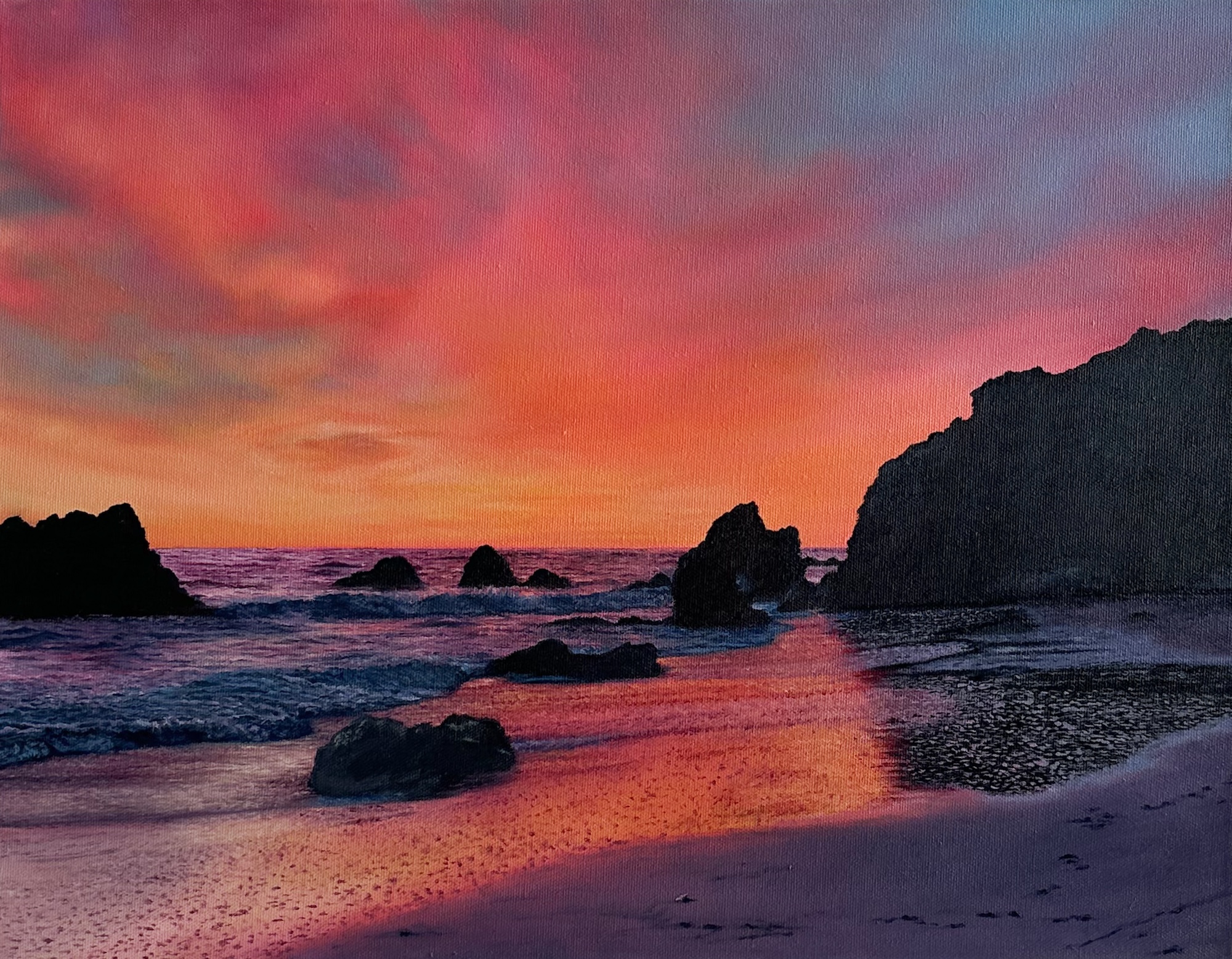 Sunset over rocky beach with vibrant pink and orange sky reflections.