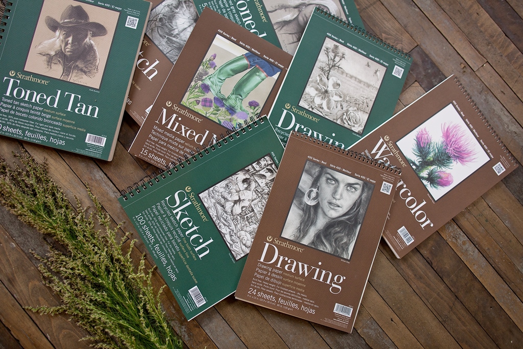 Variety of Strathmore sketchbooks on a wooden surface.